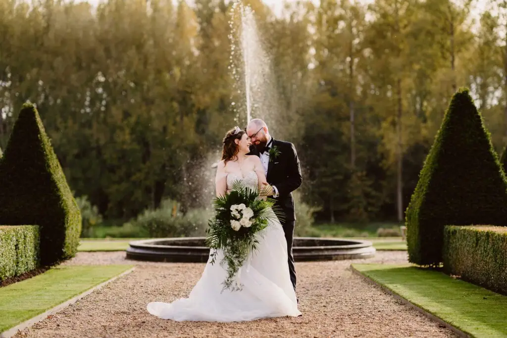 The happy couple pose for a photo in front of the water fountain at Oxnead Hall in Norfolk