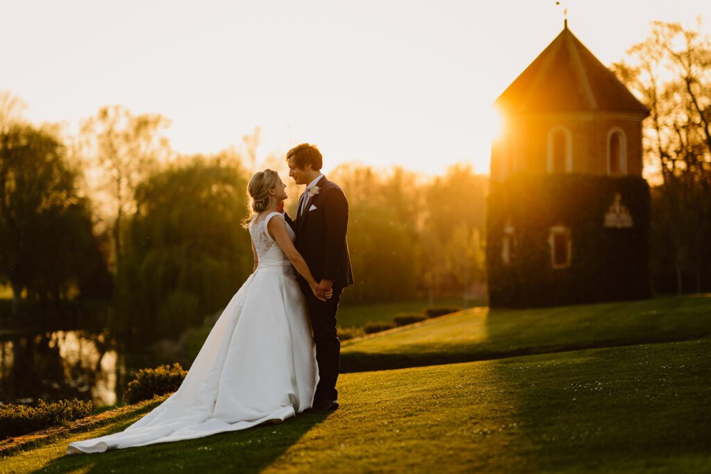 Bride and Groom standing outside Oxnead Hall with sunset behind them