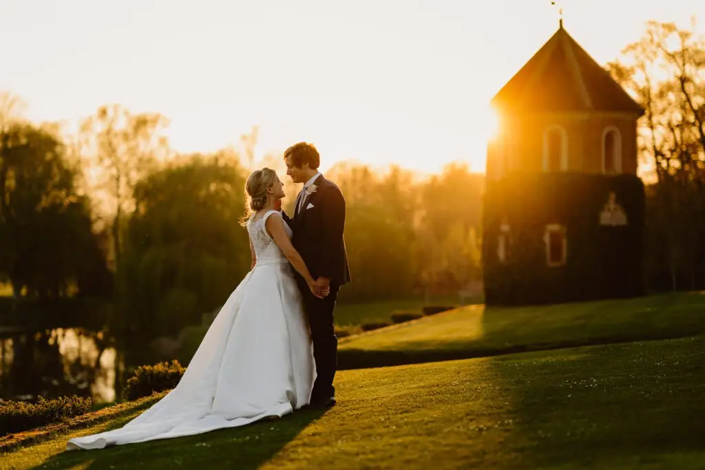 Bride and Groom standing outside Oxnead Hall with sunset behind them